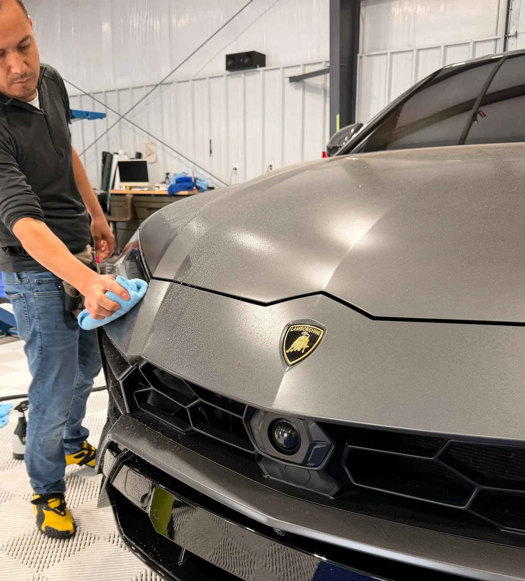Quality Window Tint installer smoothing paint protection film on the hood of a gray Lamborghini Urus